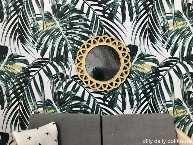 miniature dollhouse mirror above a sofa against planty wallpaper